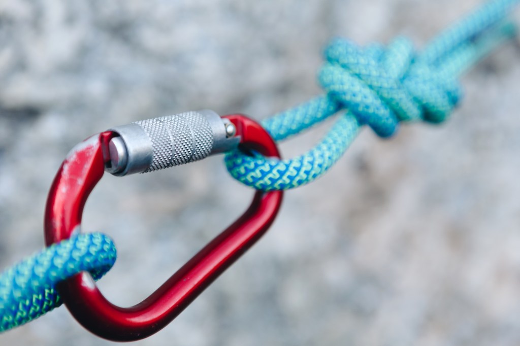 red carabiner holding blue climbing ropes